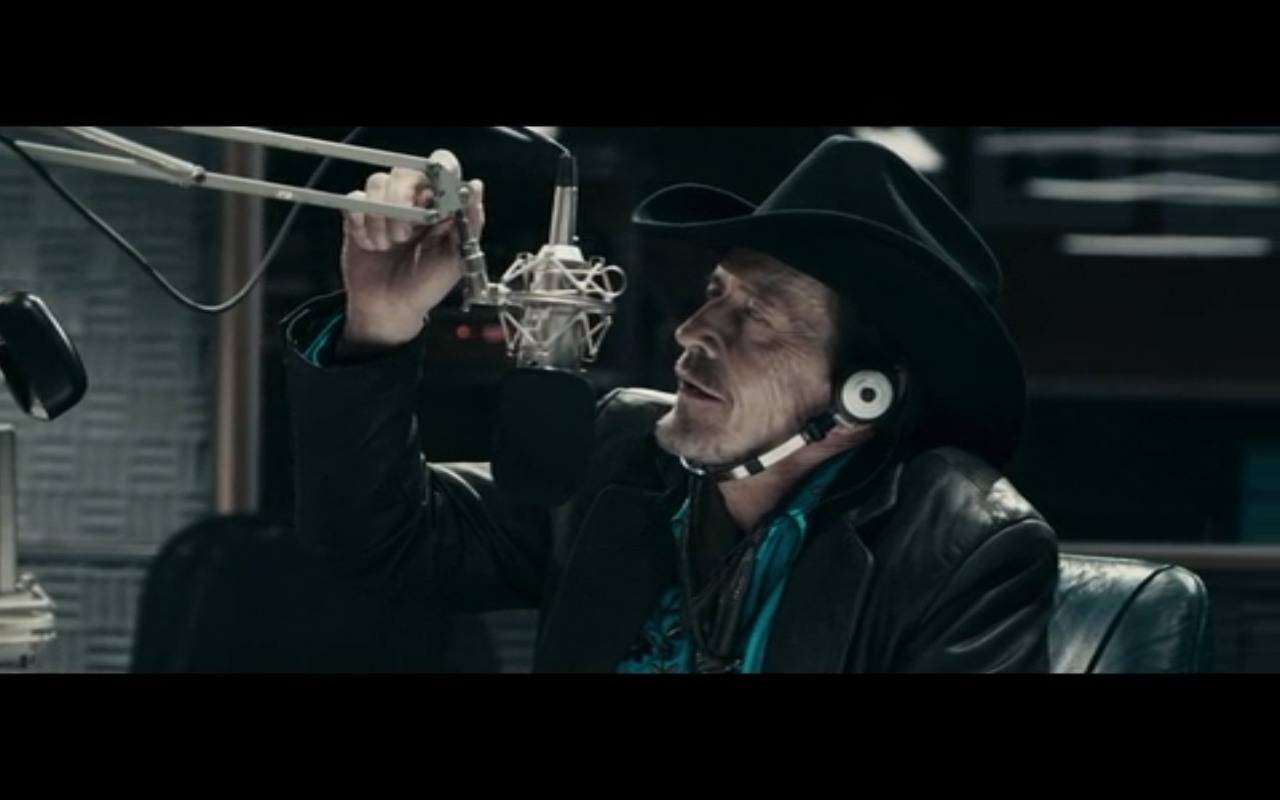 A man recording a radio show wears a cowboy hat and speaks into a microphone