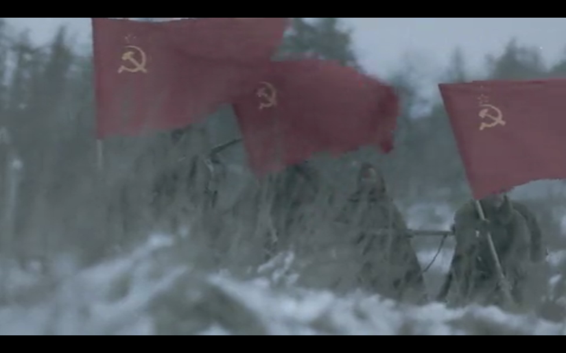 Soldiers march in the snow while carrying red flags with the Soviet Union's hammer and sickle