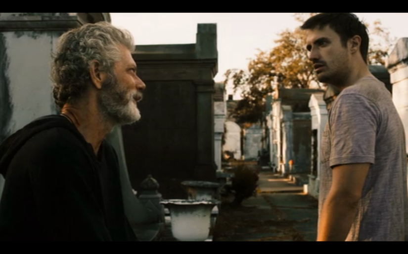 An older man talks to another man in an elegant cemetery.