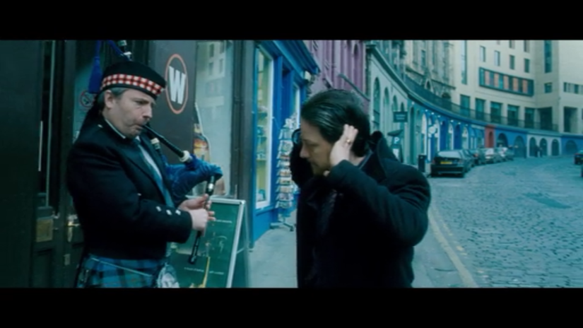 A man covers his ears as he passes another man playing bagpipes on a street corner