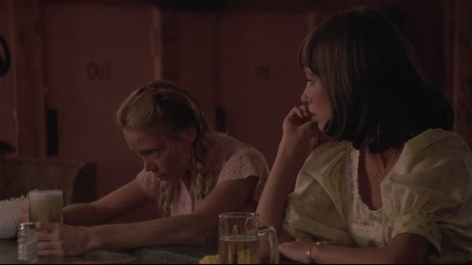 two women sit at a bar with pints of beer