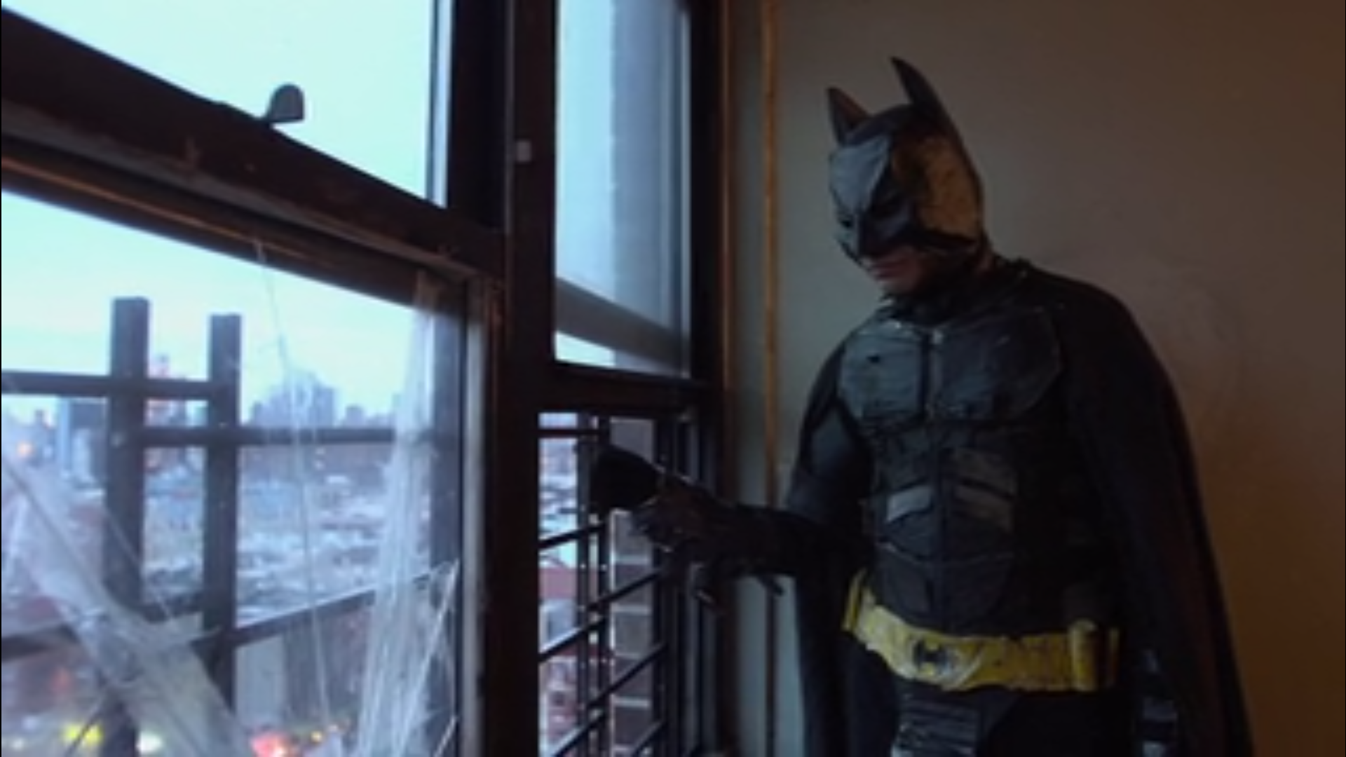 a teenage boy looks out of an apartment window, dressed in a detailed Batman costume