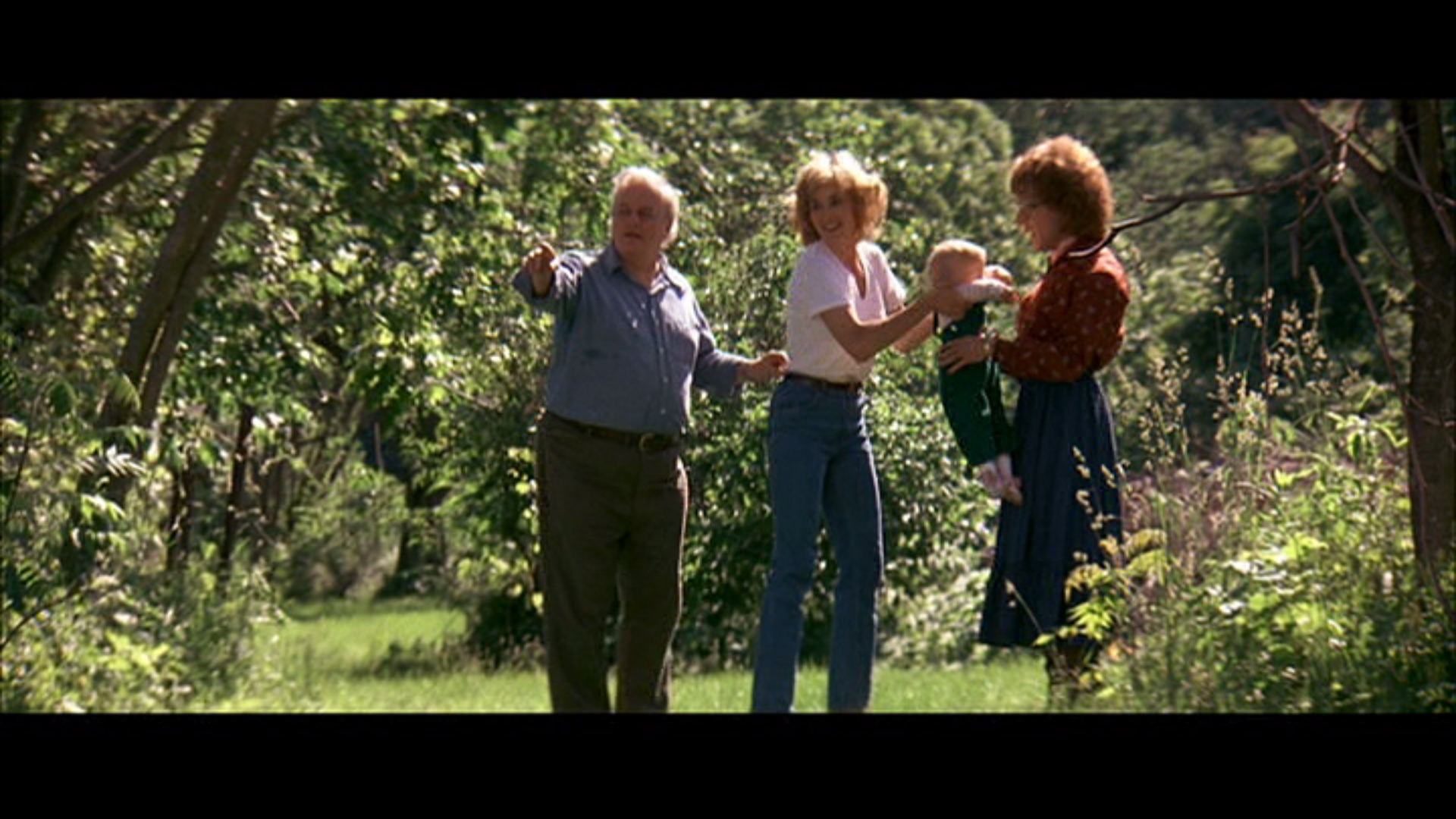 an older man and two women stand in a wooded area with a toddler