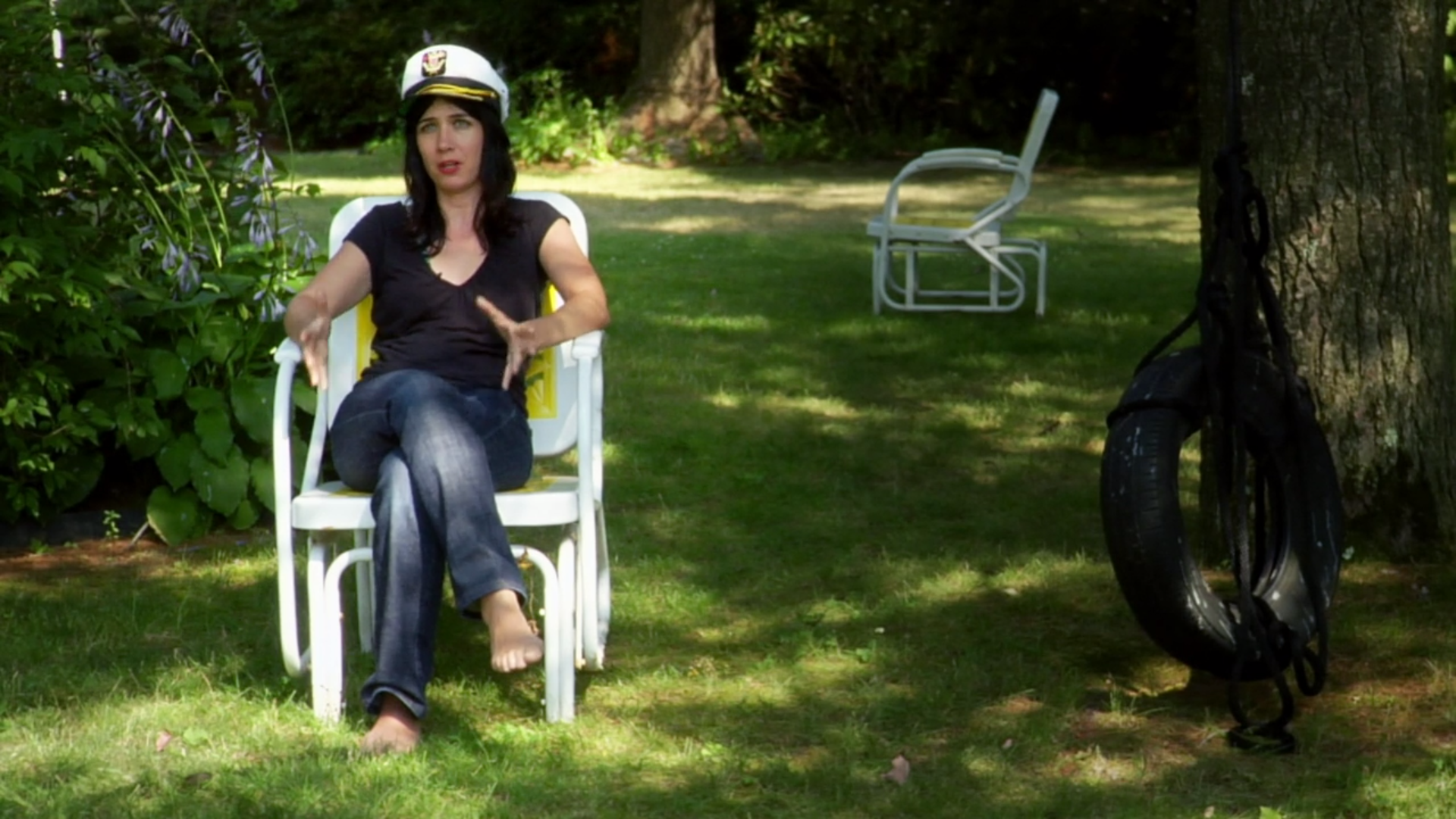 A woman sits outside in a chair, wearing a sailor hat.
