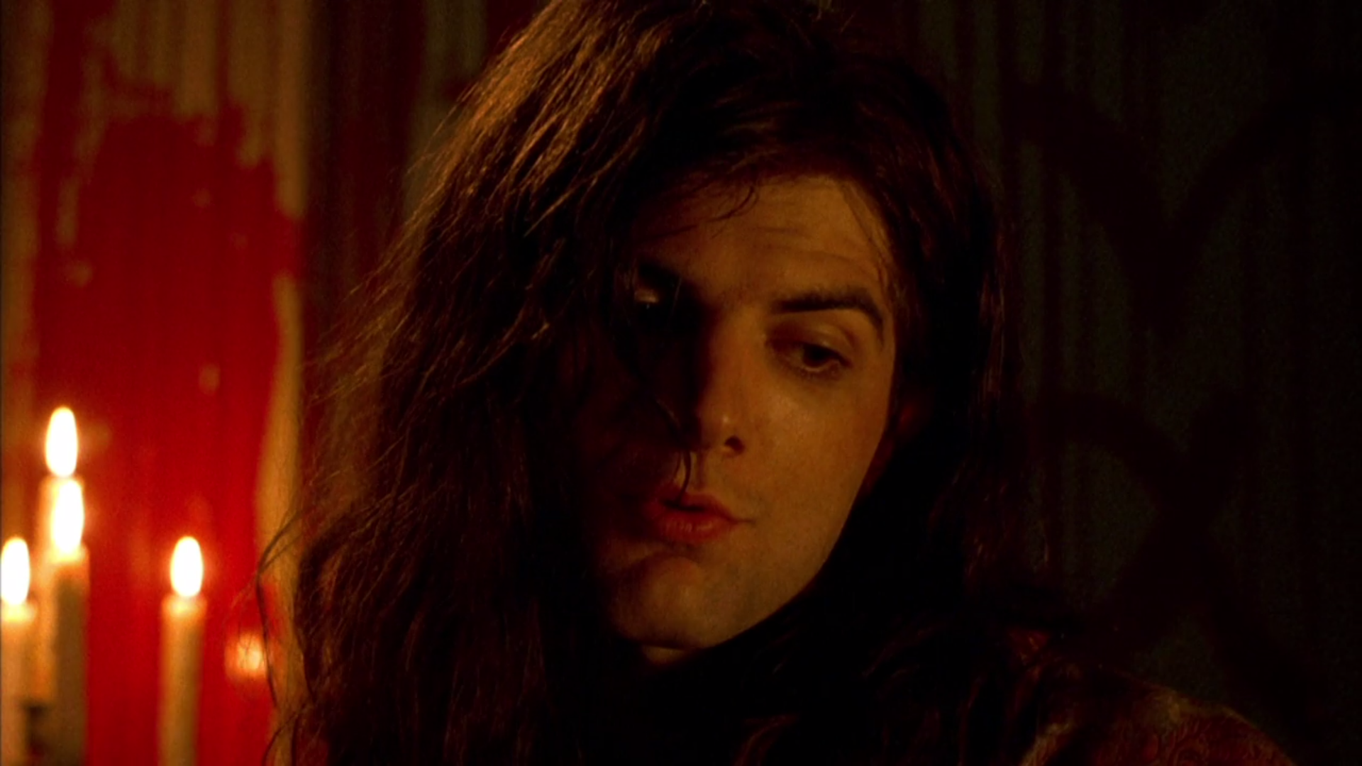 Actor Adam Scott has extremely long, flowing hair, and stands in a candelit room.