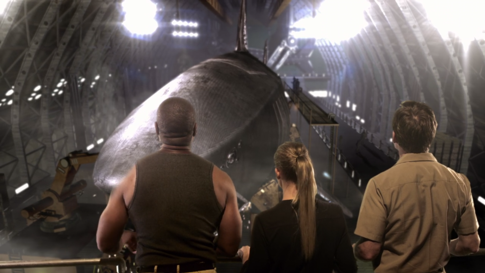 Three people look down at a large metallic shark under construction.