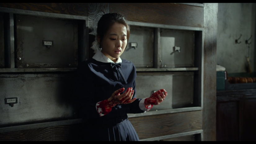 a teen girl in a school uniform looks in horror at her blood-covered hands