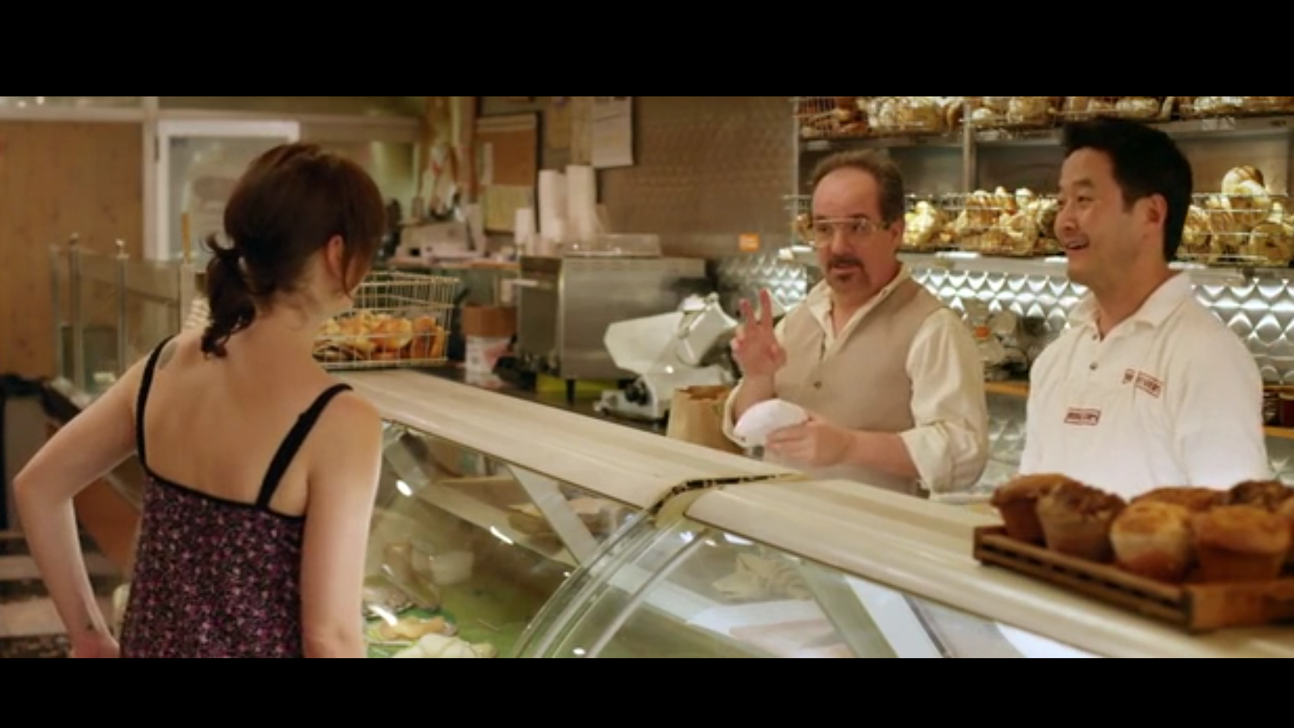 A woman in a deli interacts with two men working behind the counter.
