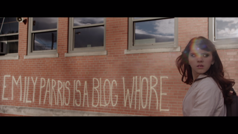 a teenage girl looks around in front of graffiti that reads "Emily Parris is a blog whore"