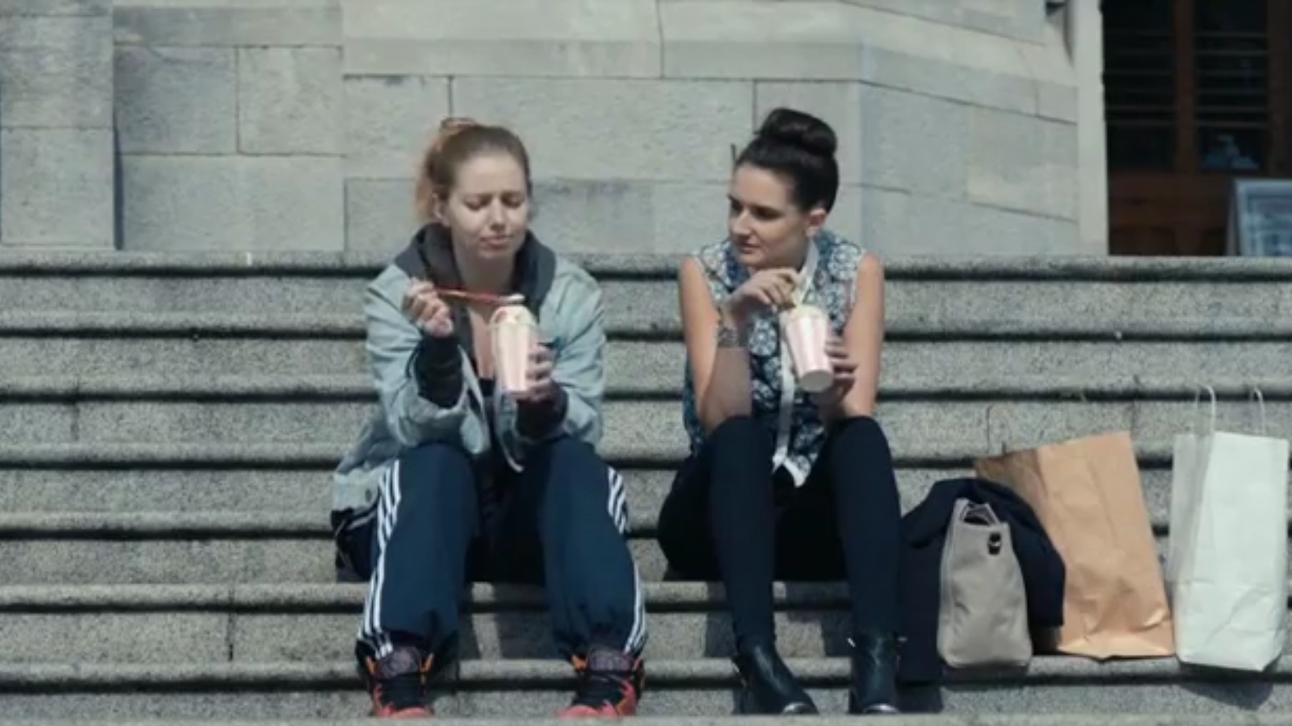 Two women sit outside on the steps of a building, eating ice cream