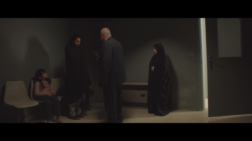 a man in a suit talks to a woman wearing a hijab, who looks down at the floor