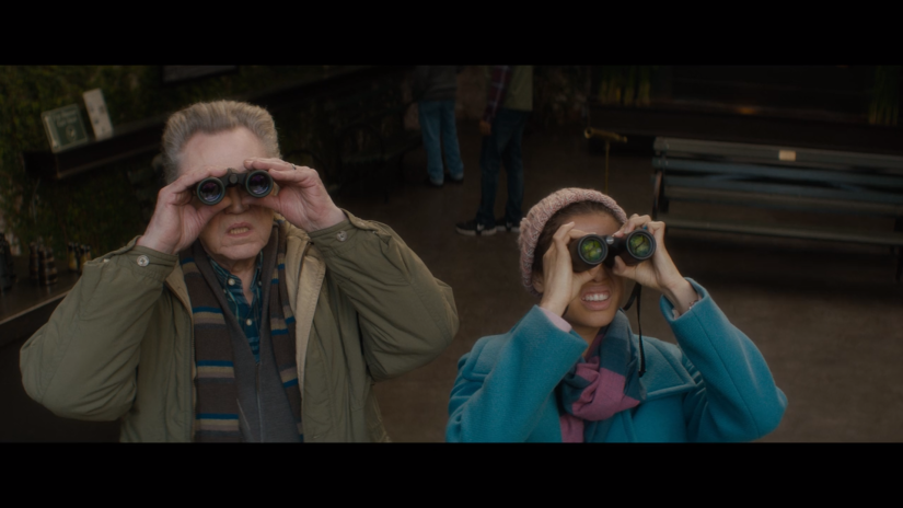 A man and woman stand next to each other, looking through binoculars.