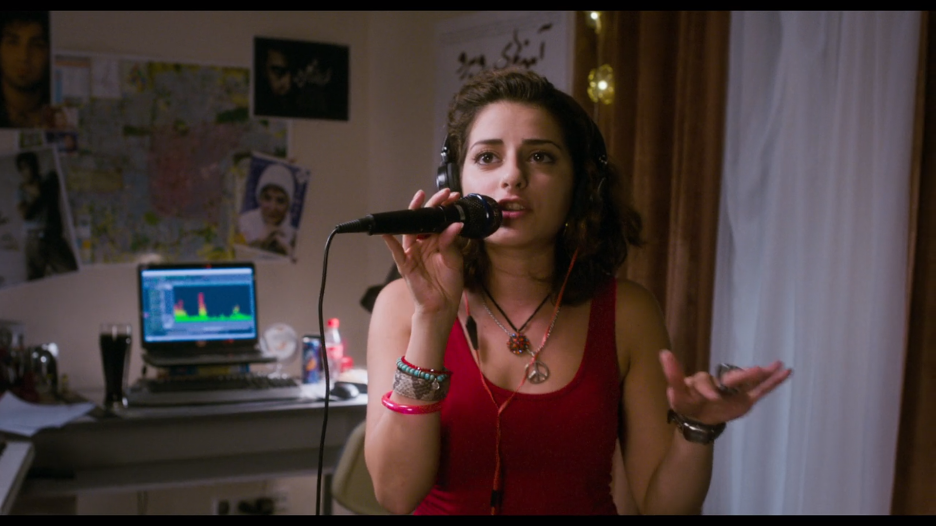 a teenage girl holds a microphone to her mouth with sound recording equipment on a computer behind her