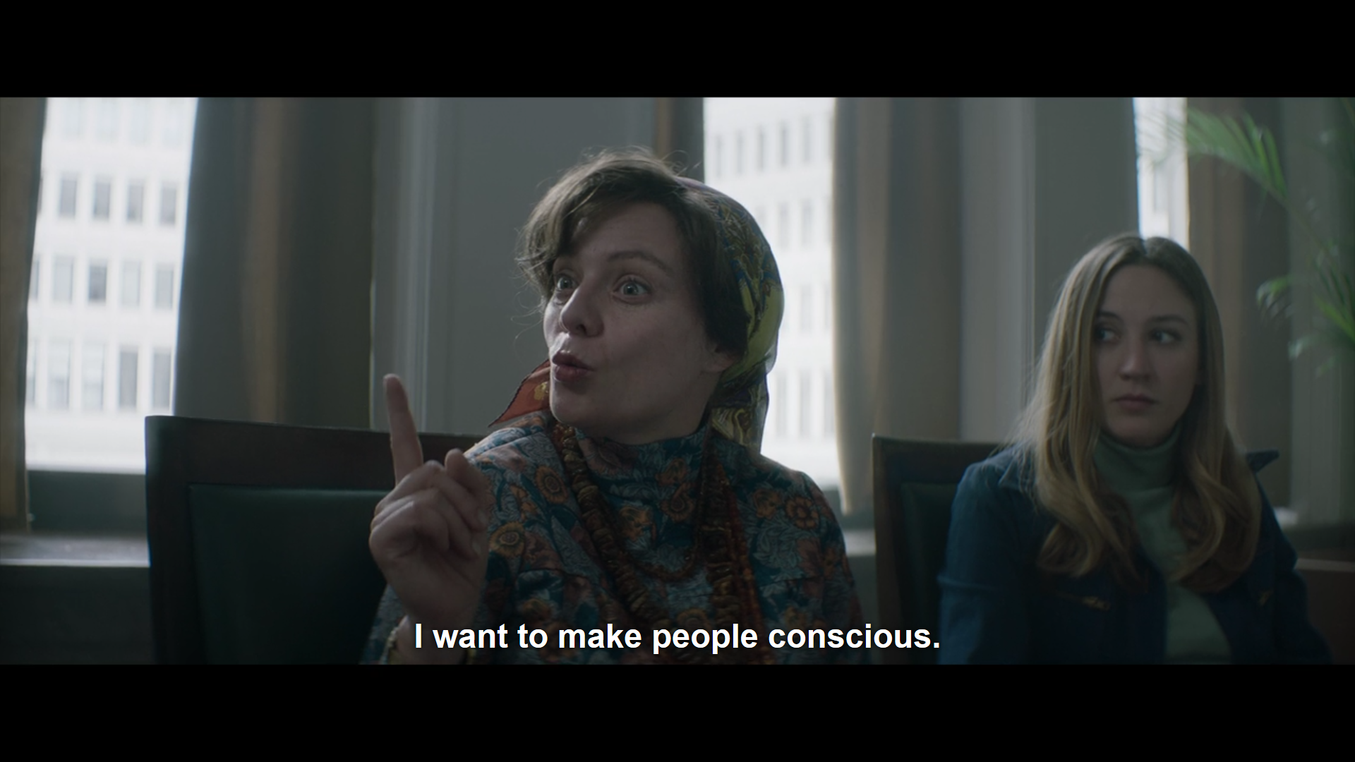 a woman wearing a headscarf is seated in a meeting room and raises her index finger as she says "I want to make people conscious"