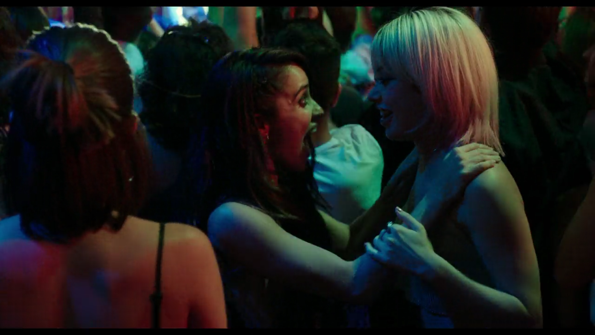 Two teenage girls at a crowded club smile excitedly at each other.