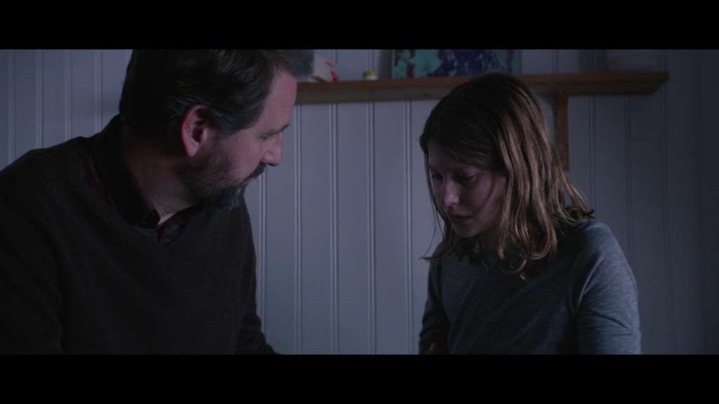 a man sits with a teenage girl in a dimly lit room