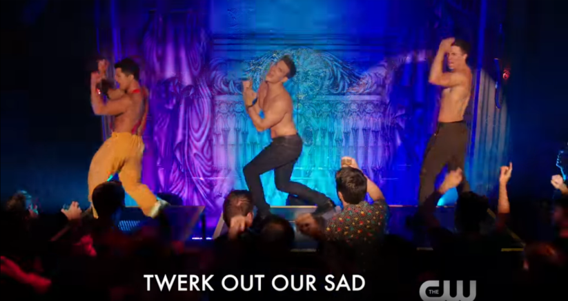 three men without shirts dance onstage in front of a crowd, singing the words "Twerk out our sad"