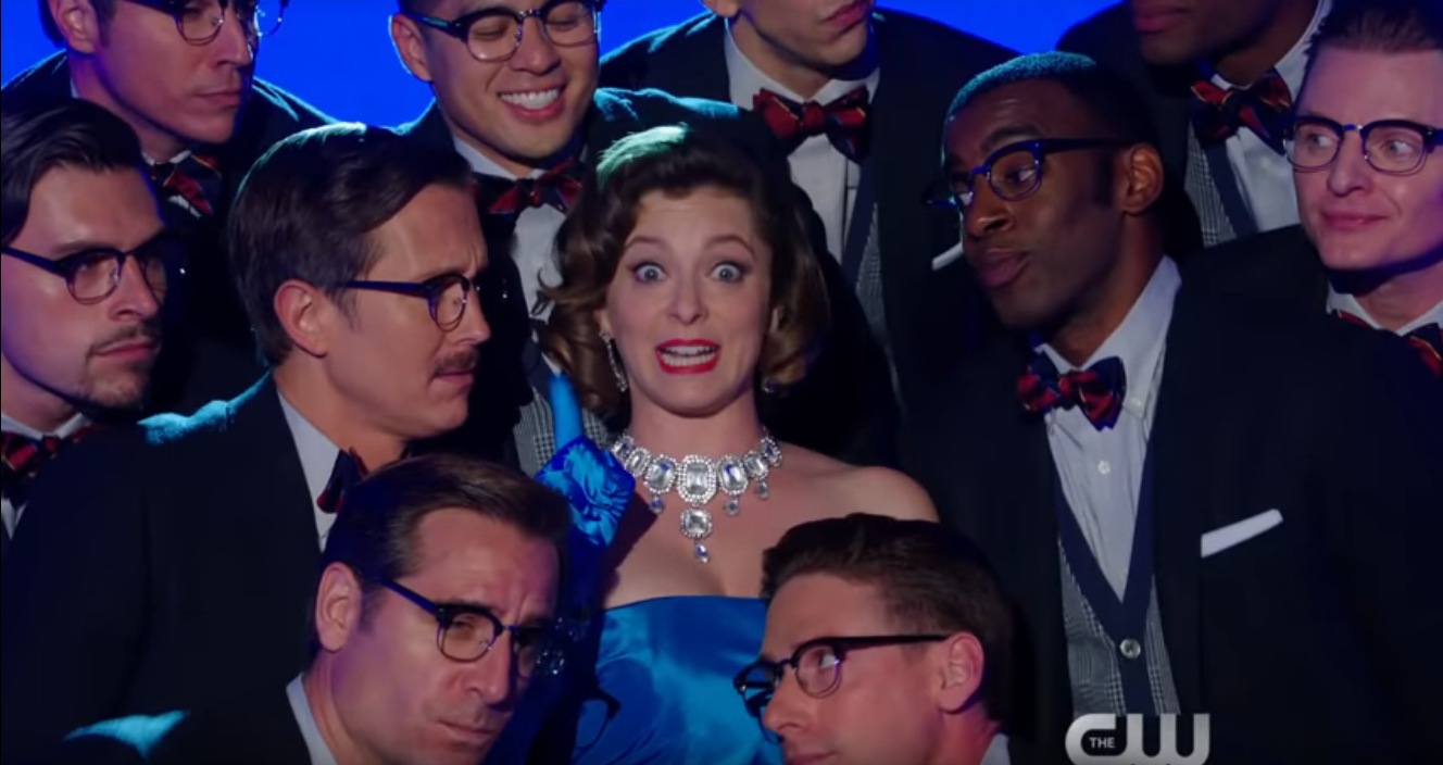 a woman in a blue dress smiles broadly as a group of men wearing glasses look on around her