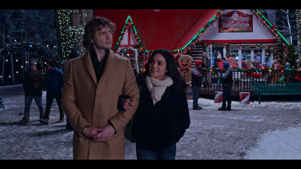 a man and woman walk through a Christmas-themed park, linking arms