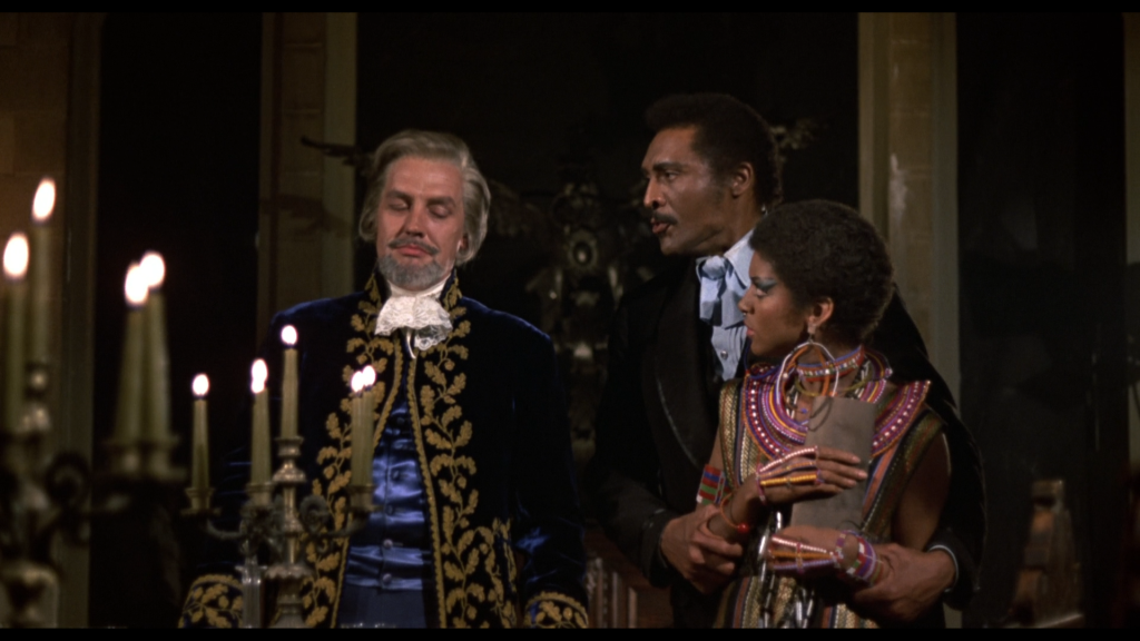 A grey-haired white man in period costume looks smug as a Black man and woman stand next to him, looking indignant.