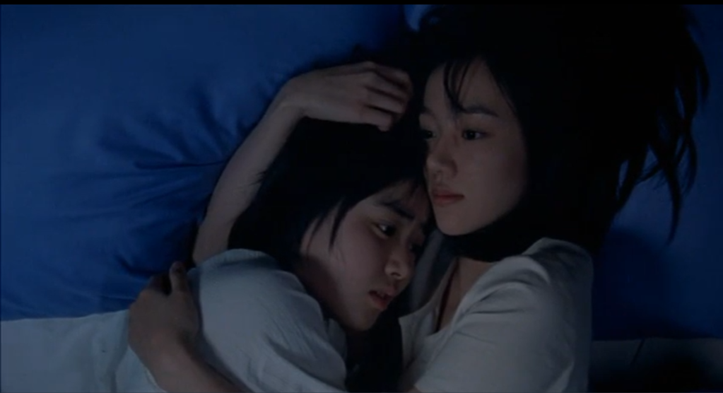 Su-mi lies in her bed with arms wrapped around Su-yeon, comforting her little sister.