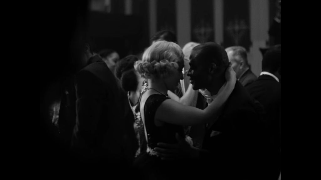 A light-skinned woman with short blonde hair dances close to a dark-skinned Black man.